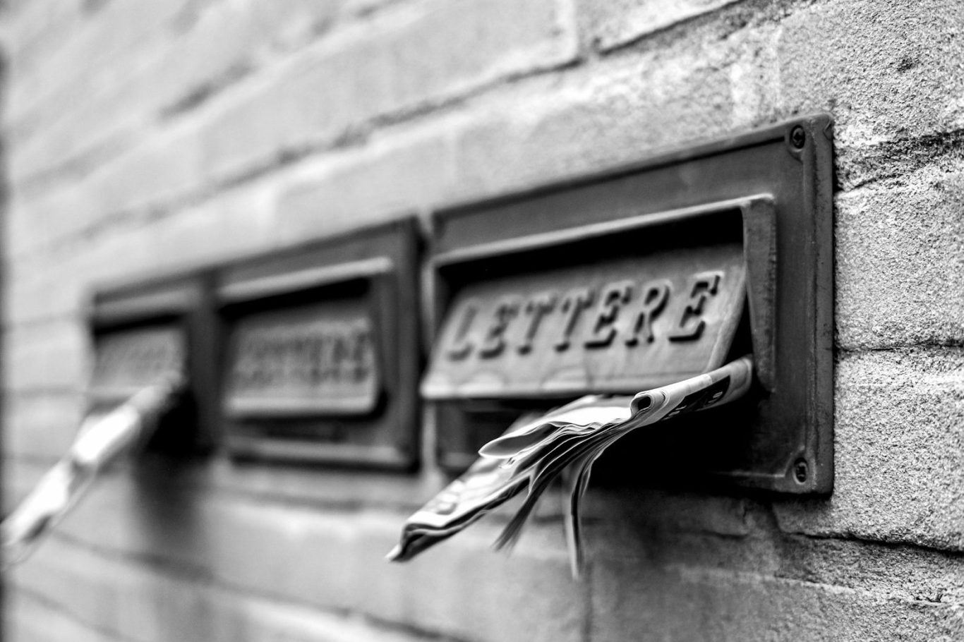 Trois boîtes aux lettres en métal avec des lettres dépassant, sur un mur de briques.