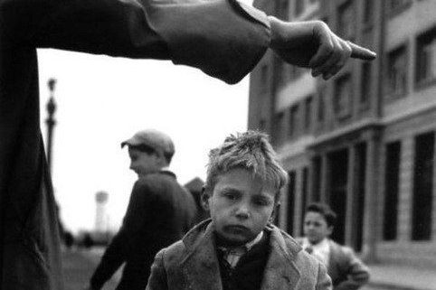 Un garçon triste avec un doigt pointé vers lui, en arrière-plan des adultes flous.