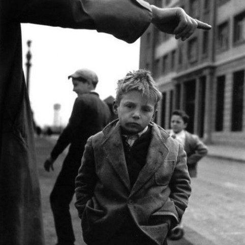 Un garçon avec un manteau, l'air pensif, devant des passants dans une rue historique.