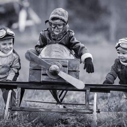 Un pilotage flexible et opérationnel Trois enfants en costume de pilote jouent avec un avion en bois.