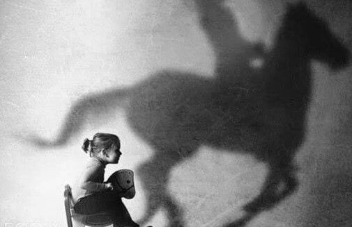 Enfant sur un cheval à bascule, projetant l'ombre d'un cavalier.