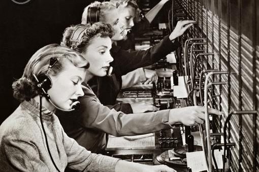 Quatre opératrices téléphoniques utilisant un central téléphonique vintage.