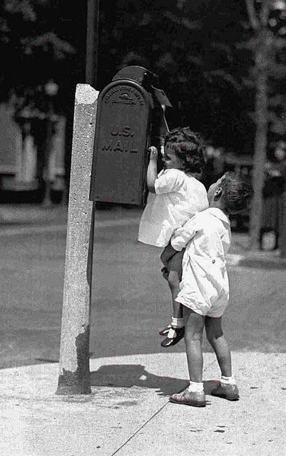 LE SENTIMENT D'ÊTRE UTILE Deux enfants, l'un portant l'autre, tentent d'atteindre une boîte aux lettres.