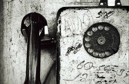 Téléphone vintage avec cadran, posé sur un mur marqué par des graffitis.