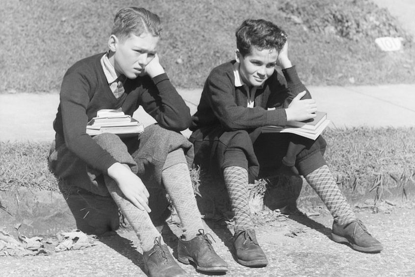 Deux jeunes garçons assis, pensifs, tenant des livres, sur le trottoir.