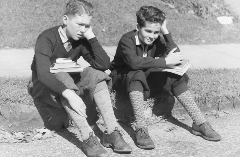 Deux garçons assis sur le sol, pensifs, avec des livres à la main.