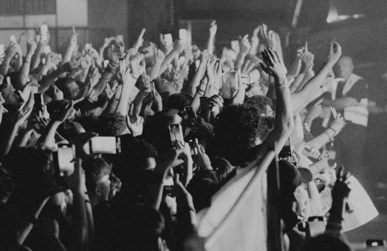 Public enjoué levant les mains lors d'un concert, ambiance festive en noir et blanc.