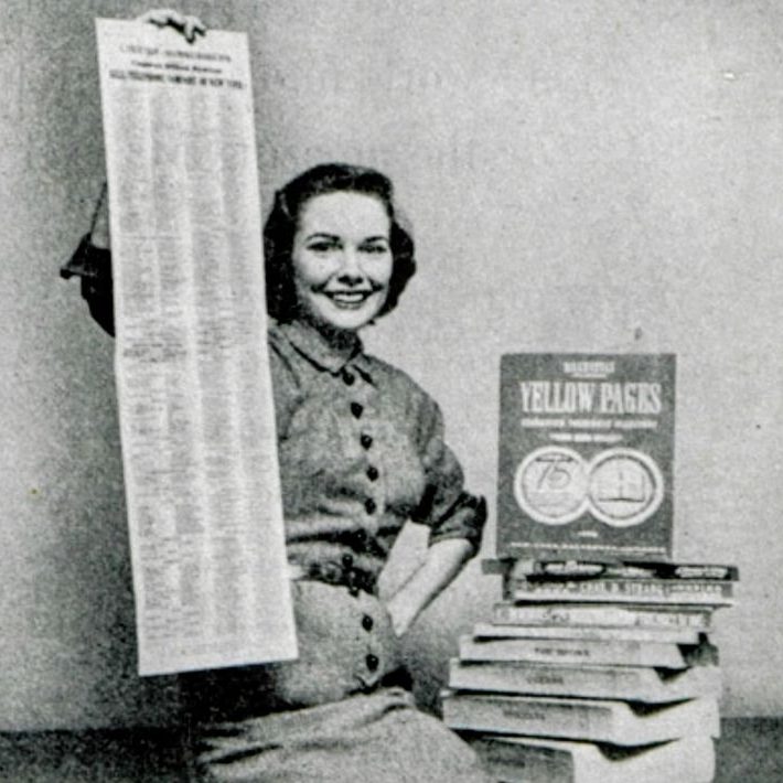 Femme souriante tenant un long document à côté de livres empilés.